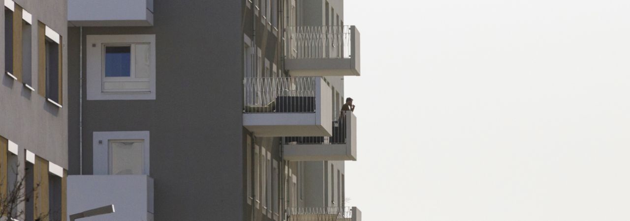 Eine Person telefoniert auf dem Balkon eines Hochhauses.